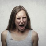 Dona jove amb expressió de ràbia, celles arrufades i mandíbula tensa, mostrant signes d'enuig i frustració.